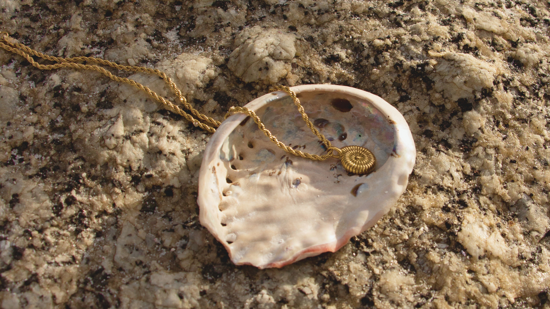 Gold shell necklace in an abalone shell on a textured rock