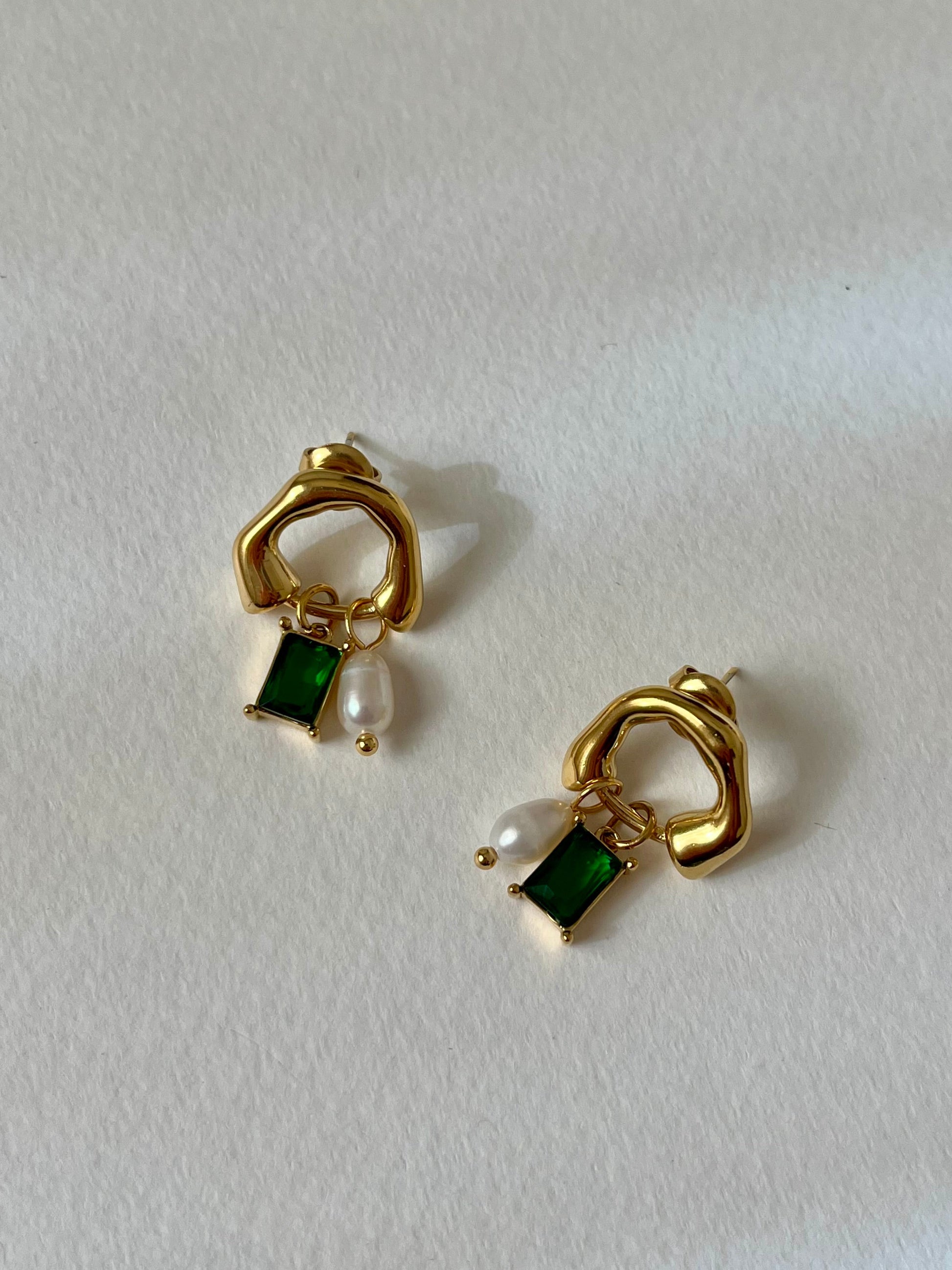 Gold earrings with green gemstones and pearls on a white background