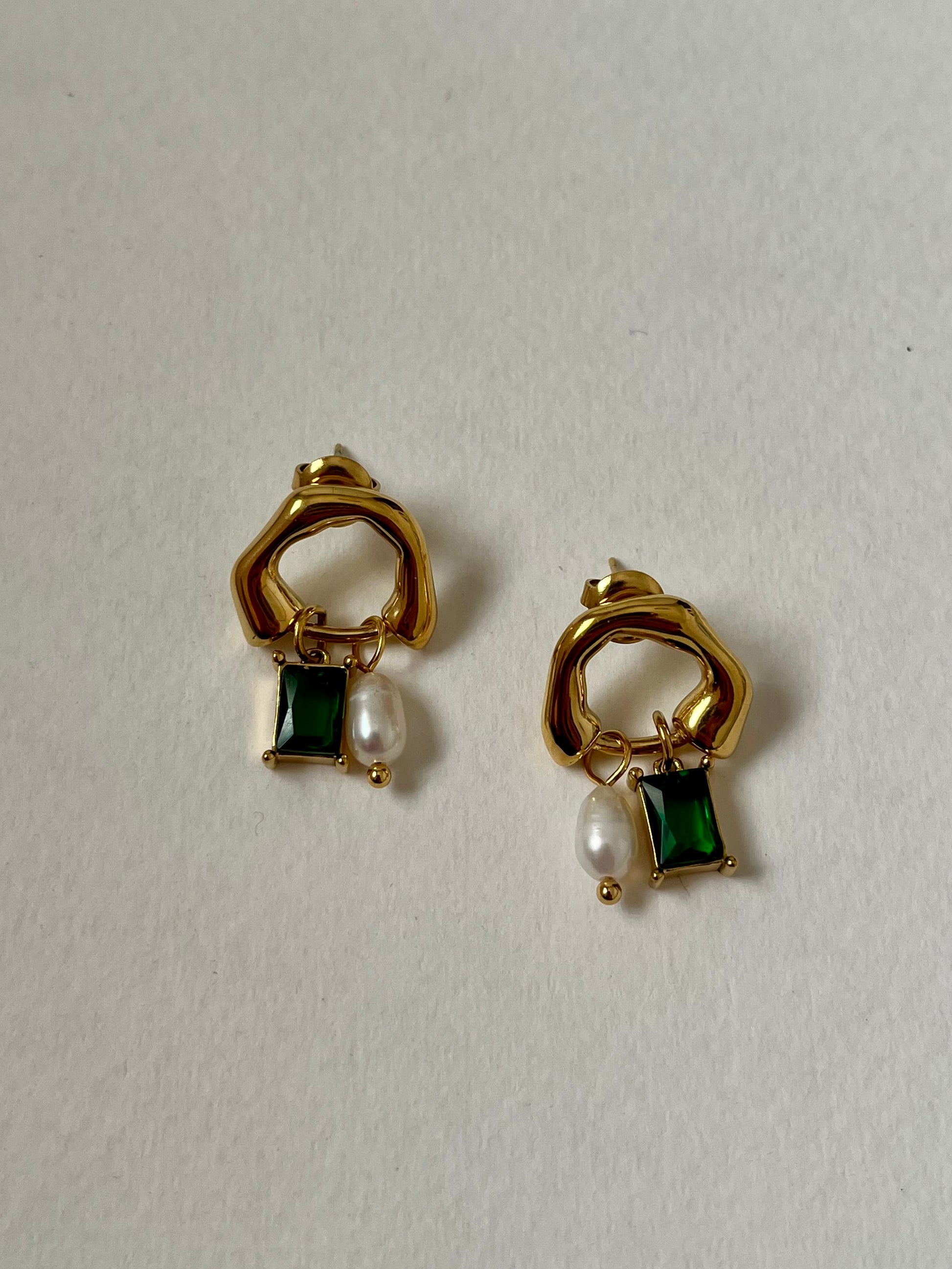 Gold earrings with green gemstones and pearls on a white background